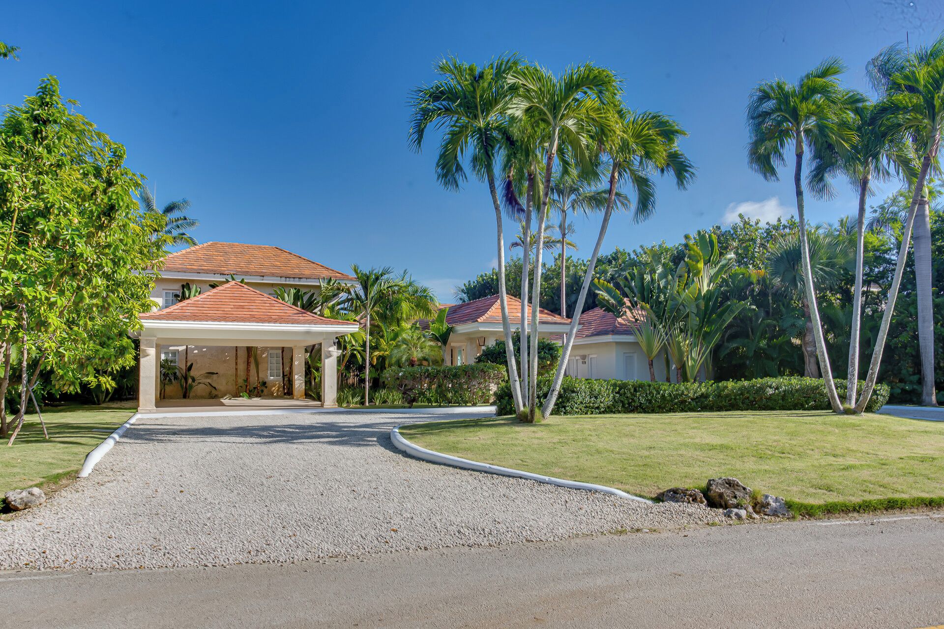 A residential property with a covered driveway, palm trees, and a well-maintained lawn.