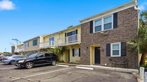 A row of townhouses with a parking lot in front, featuring a brick facade and a balcony on the second unit. - Island Breeze at Islander Cay (Myrtle Beach)