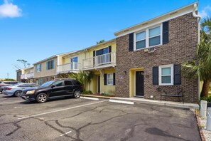 A row of townhouses with a parking lot in front, featuring a brick facade and a balcony on the second unit. - Island Breeze at Islander Cay (Myrtle Beach)