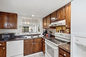 A kitchen with wooden cabinets, a microwave, a dishwasher, a stove, and a sink. - Island Breeze at Islander Cay (Myrtle Beach)
