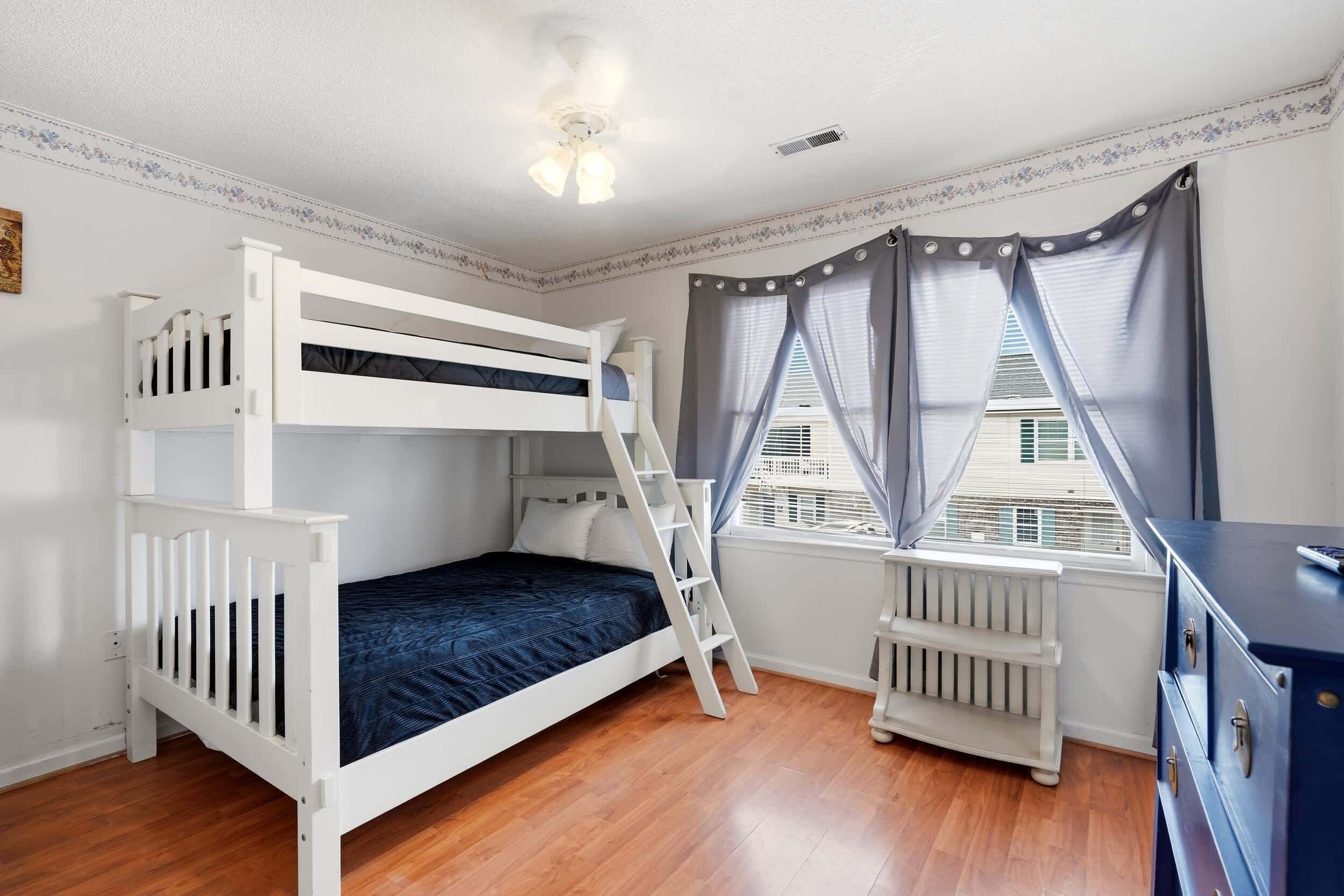 A bunk bed room with a ladder, a radiator, and a window with curtains.