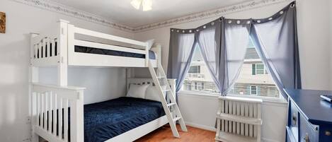 A bunk bed room with a ladder, a radiator, and a window with curtains.