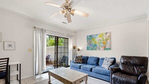 A living room with a blue sofa, a wooden coffee table, a black leather chair, and a ceiling fan. - Island Breeze at Islander Cay (Myrtle Beach)