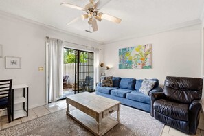 A living room with a blue sofa, a wooden coffee table, a black leather chair, and a ceiling fan. - Island Breeze at Islander Cay (Myrtle Beach)
