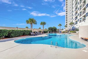 A swimming pool with lounge chairs and palm trees, surrounded by a high-rise building. - Myrtle Beach Resort Ocean View Condo (Myrtle Beach)