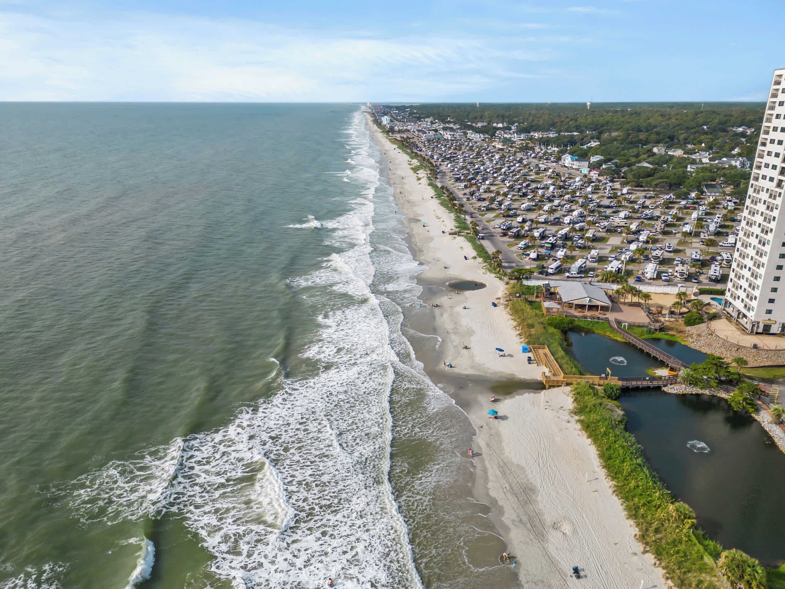 A coastal area with a beach, a parking lot, and a large building.