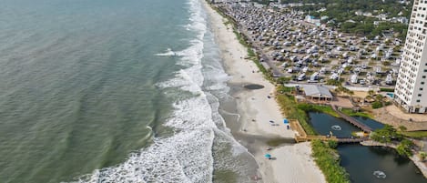 A coastal area with a beach, a parking lot, and a large building.