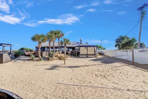 Une propriété située en bord de mer, comprenant une maison, des palmiers et un filet de volleyball.