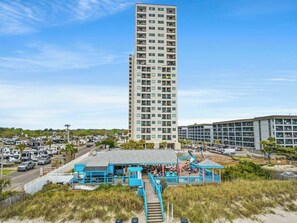 A high-rise building with multiple floors, a beachside restaurant with outdoor seating, and a parking area with RVs. - Myrtle Beach Resort Ocean View Condo (Myrtle Beach)