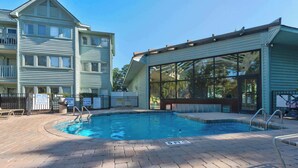 A swimming pool with a brick deck, surrounded by a building with large windows and a covered area. - Myrtle Beach Resort Ocean View Condo (Myrtle Beach)