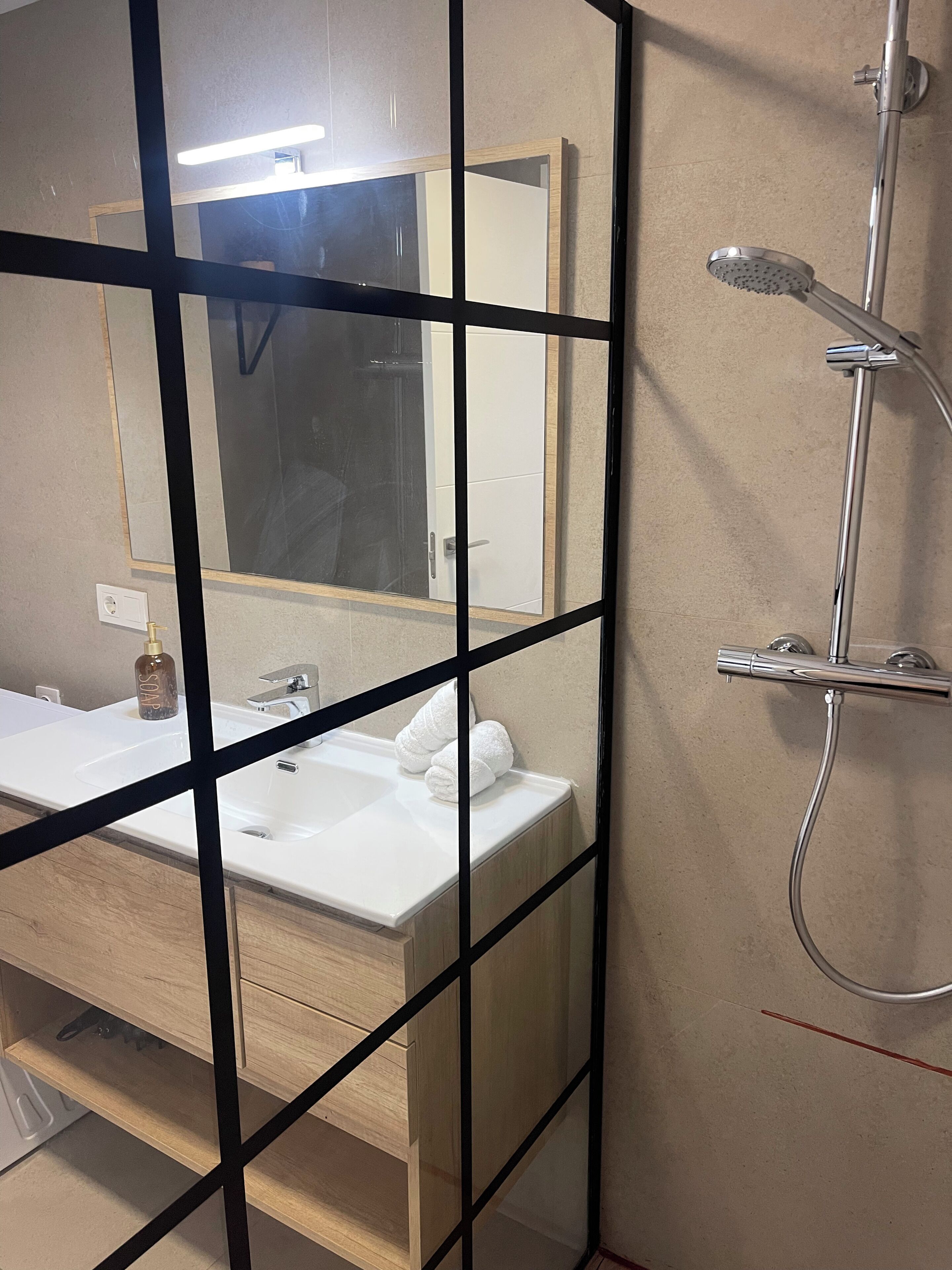 A bathroom with a white sink, a mirror, a shower, and a towel rack.