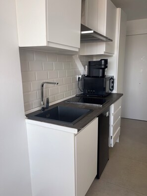 Et moderne køkken med hvide skabe, en sort bordplade, en integreret vask og en kaffemaskine.