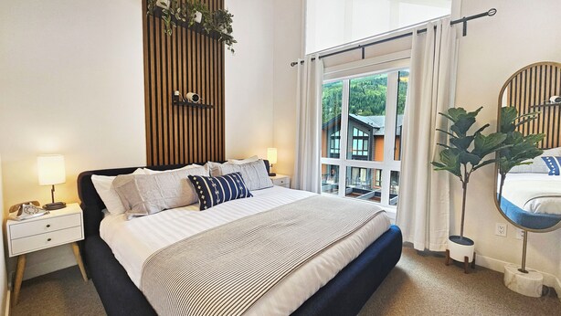 Hotelkamer met een groot bed, nachtkastje met een lamp, spiegel en uitzicht op een gebouw.