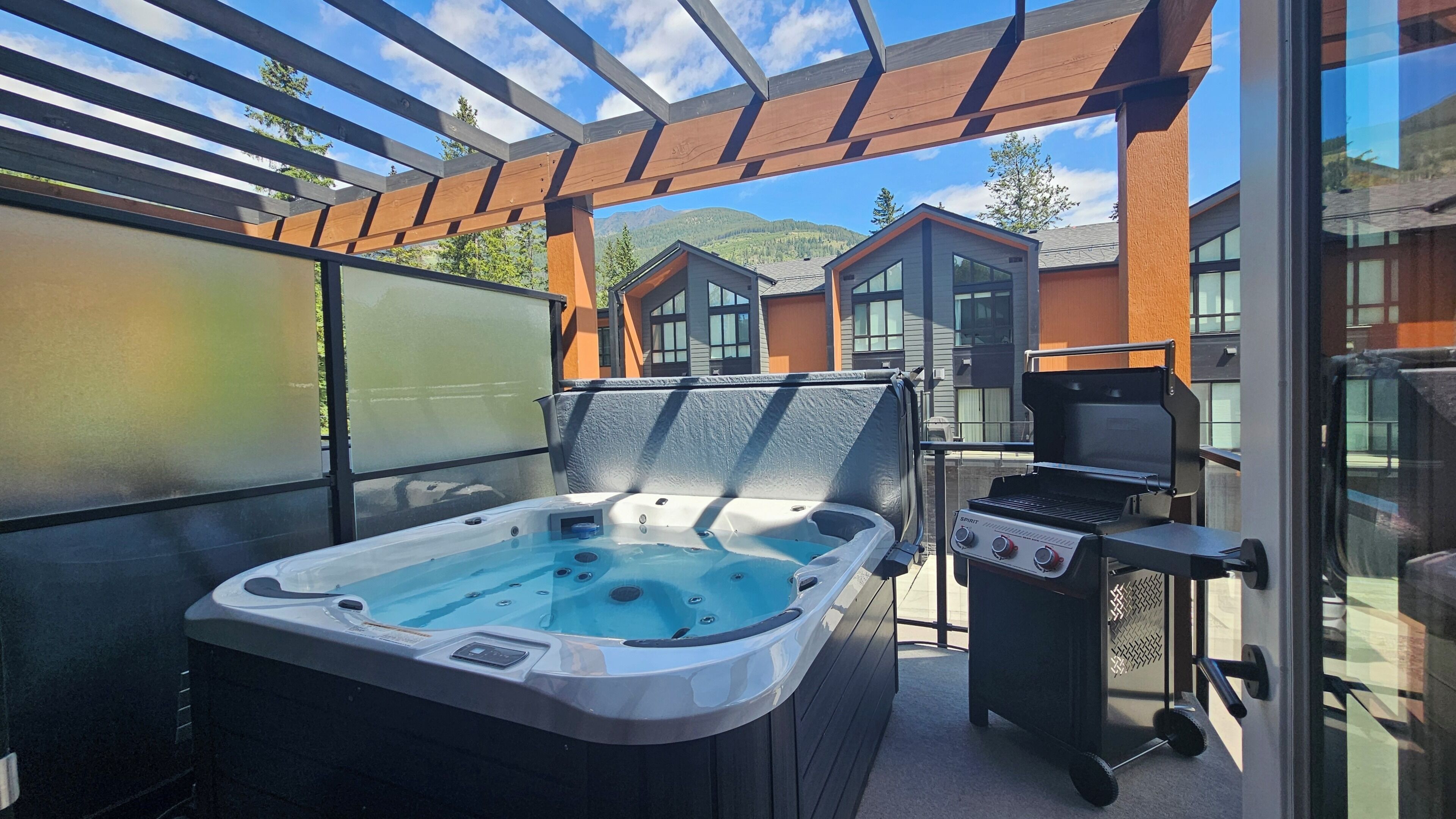 A hot tub and grill on a covered patio with a view of buildings and mountains.