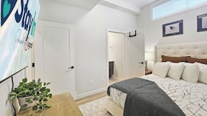 Ein modernes Schlafzimmer mit einem großen Bett, einem Nachttisch, einer Lampe und einem an der Wand montierten Fernseher.