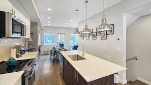 Een moderne keuken met een centraal eiland, roestvrijstalen apparatuur en hanglampen.