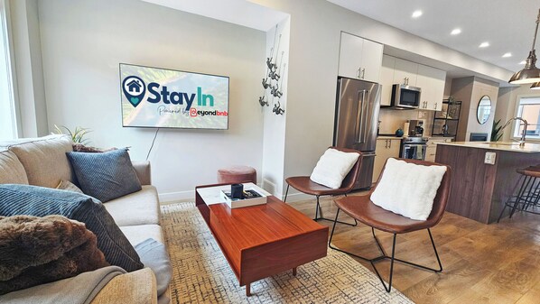 A modern living room with a sofa, coffee table, and a TV mounted on the wall displaying a 'StayIn' sign. - Pet-Friendly Panorama Escape / Hot Tub / Sleeps 10 (Panorama)
