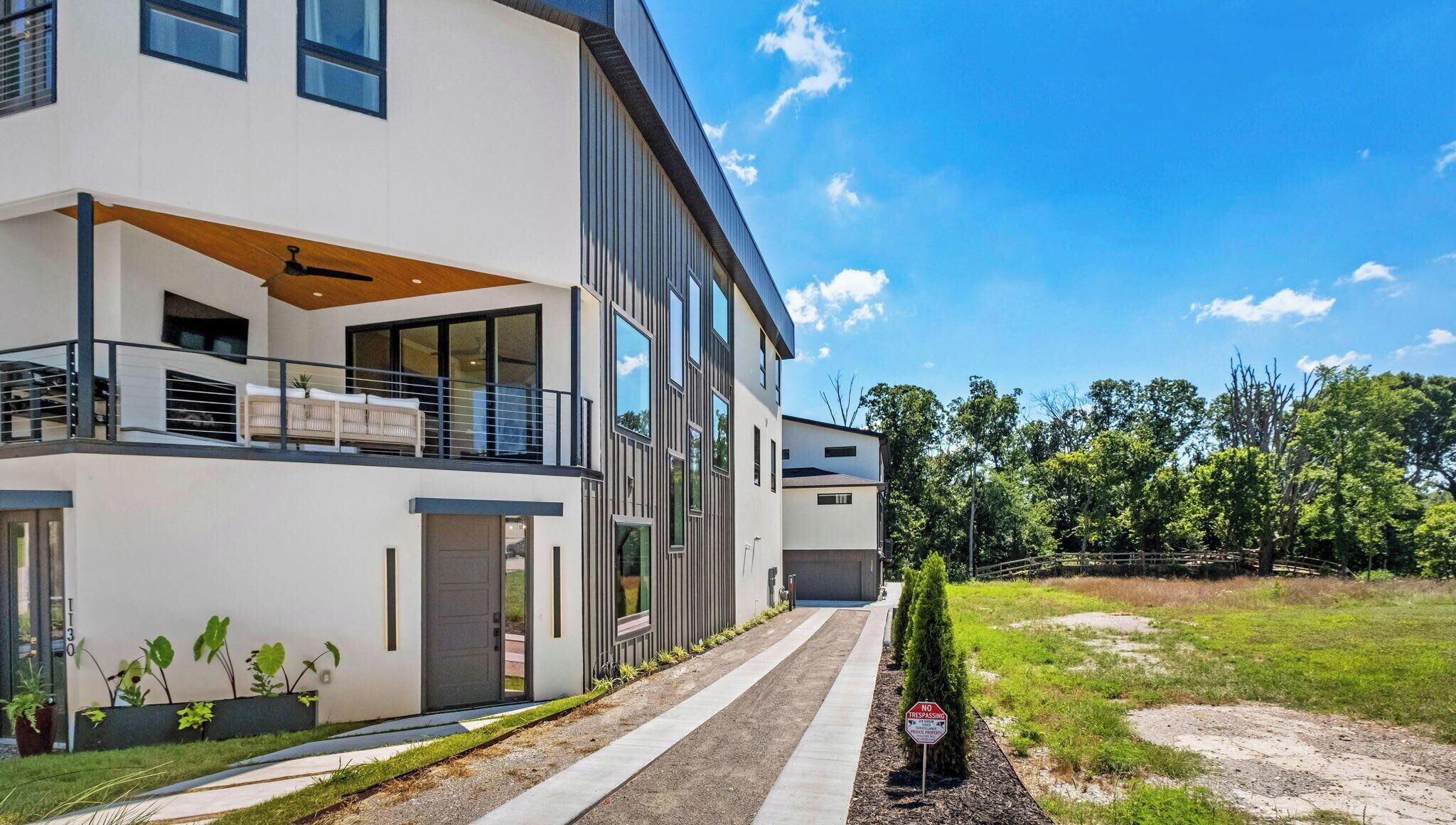A modern two-story house with a balcony, a driveway, and a 'No Trespassing' sign.