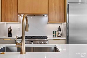 A modern kitchen with stainless steel appliances, a double sink, and wooden cabinets. - Slaughter Pen Flow-Hub Trail House (Bentonville)
