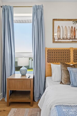 A bedroom with a wooden headboard, a bedside table with a vase, and a view through curtains to the outside. - Beach Vibes Flow-Hub Trail Access House! (Bentonville)