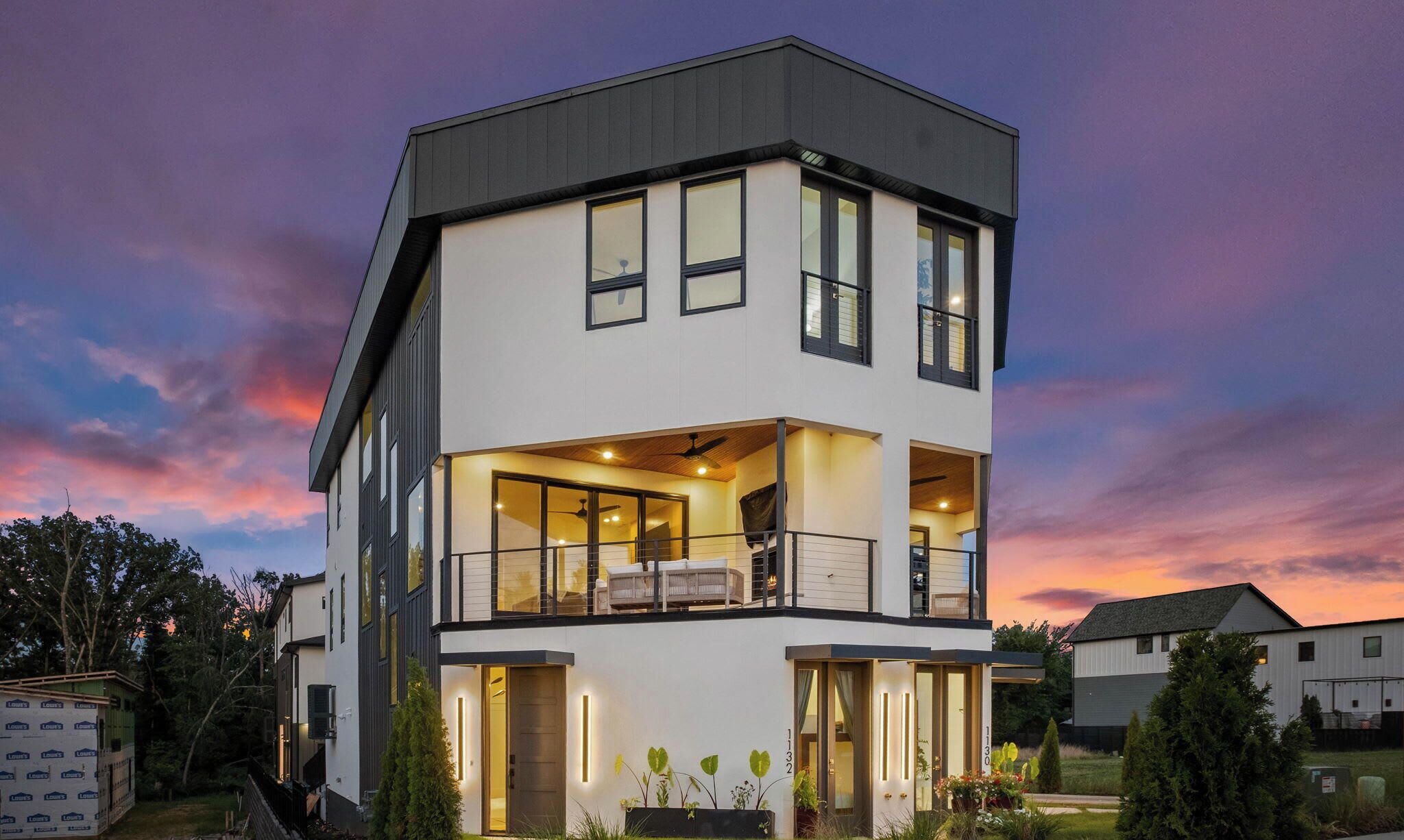 A modern two-story house with a balcony, large windows, and a well-lit entrance.