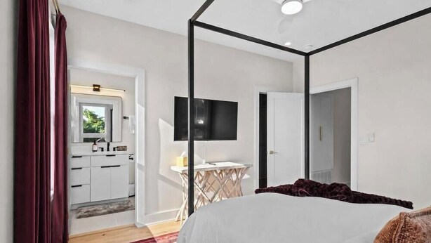Ein Schlafzimmer mit Himmelbett, Schreibtisch und Flachbildfernseher, mit Blick auf eine Küche und ein Badezimmer durch eine geöffnete Tür.