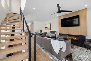 Ein modernes Wohnzimmer mit Treppe, Flachbildfernseher, Kamin und Essbereich.