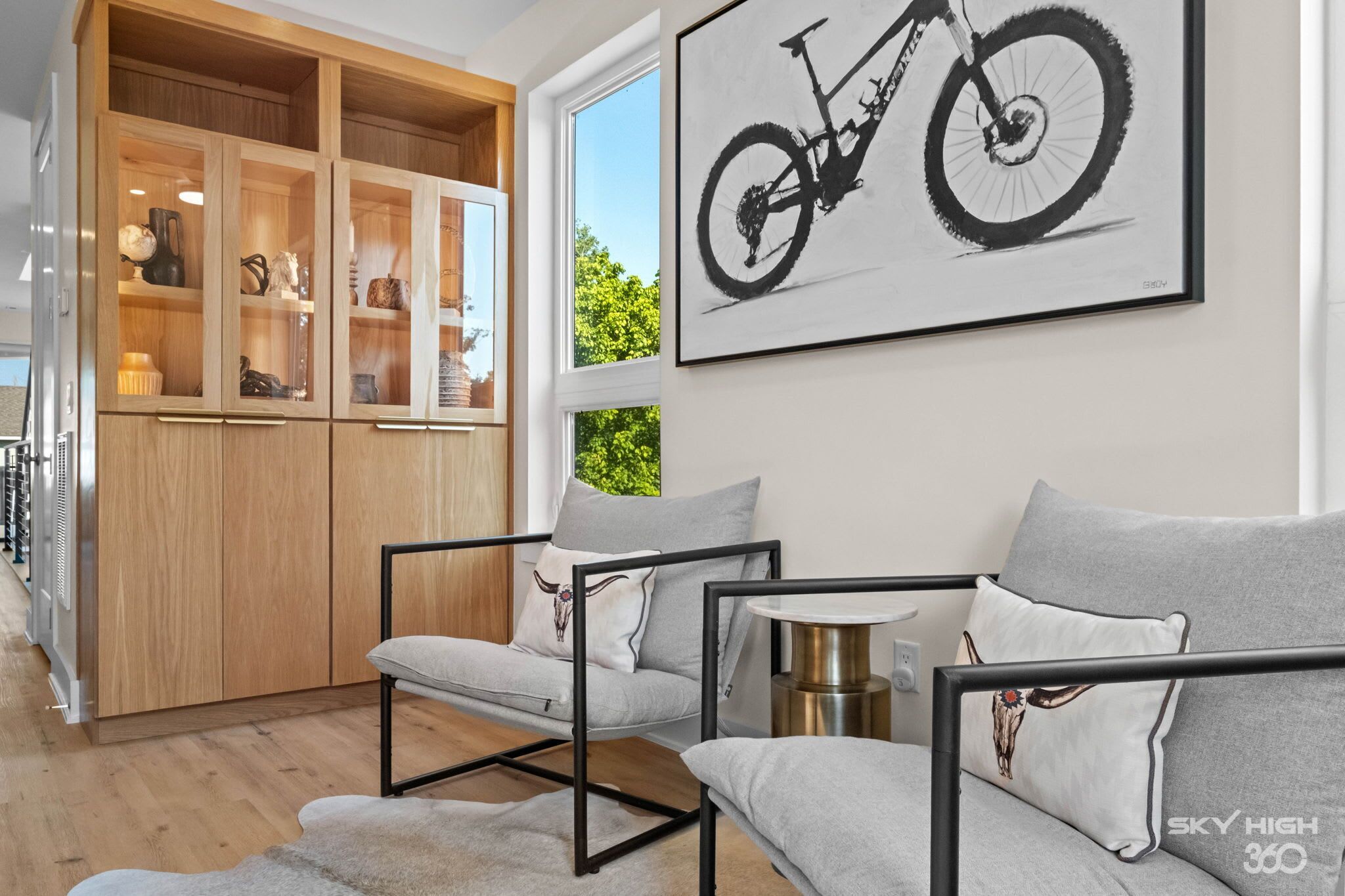 Una sala de estar moderna con un conjunto de sofás, un mueble de madera con puertas de cristal y una obra de arte con un cuadro de bicicleta en la pared.
