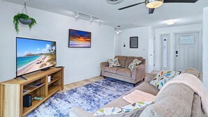 Ein Wohnzimmer mit Fernseher, Deckenventilator, Sofa und Teppich.