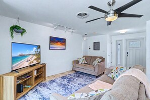 Ein Wohnzimmer mit Fernseher, Deckenventilator, Sofa und Teppich.