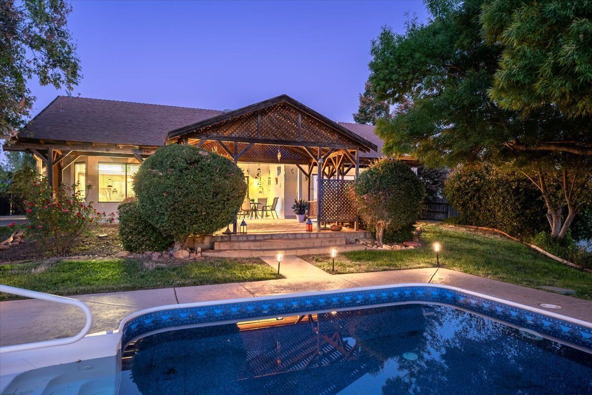 A house with a swimming pool, a covered patio, and a well-maintained garden.