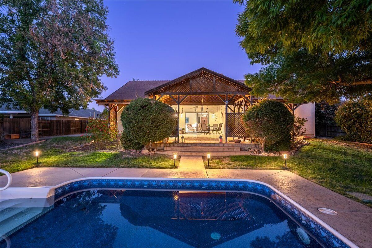 A residential property with a swimming pool, a covered patio, and a well-maintained lawn.