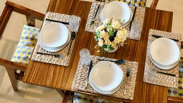 Een eettafel gedekt met witte borden, bestek en geweven placemats.