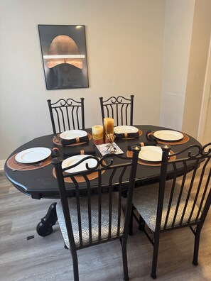 A dining table with four chairs, a candle, and a framed picture on the wall.