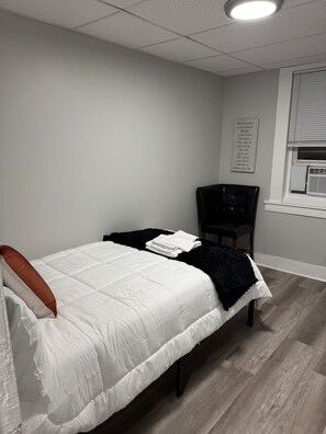 A bedroom with a bed, a chair, a window with blinds, and a motivational quote on the wall.