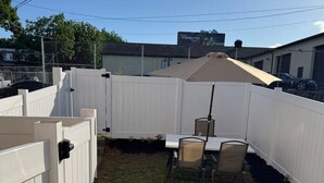A fenced backyard with a table and chairs, a concrete path, and a billboard in the background. - 2-Car Parking | Private Yard | Near I-95 (Philly) (Chester)