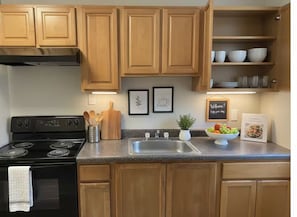 A kitchen with wooden cabinets, a black stove, a granite countertop, a sink, and various kitchen utensils.