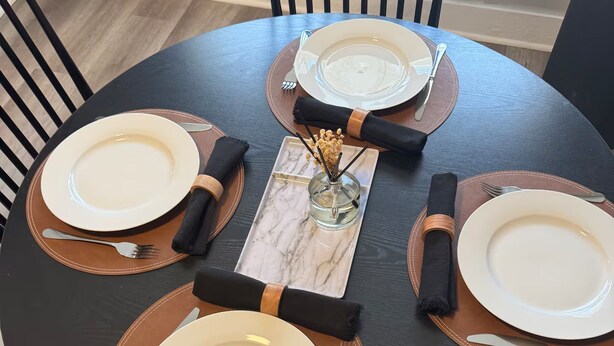A round dining table with four white plates, black napkins, and a central decorative piece. - 2-Car Parking | Private Yard | Near I-95 (Philly) (Chester)