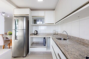 A modern kitchen with a built-in refrigerator, a sink, and a countertop with a kettle. - Apto com Churrasqueira a 400m da Praia Gravat (Navegantes)
