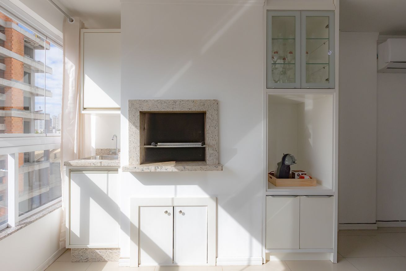 A modern kitchen with a built-in oven, white cabinetry, and a window overlooking a cityscape.