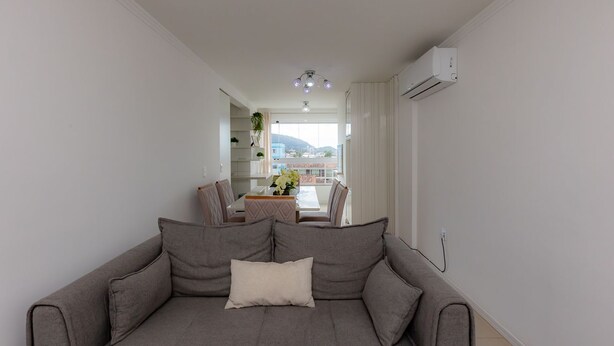 Una sala de estar moderna con un sofá gris, un comedor con mesa y sillas, y vistas al exterior.