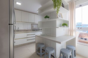 A modern kitchen with white cabinetry, a built-in stove, and a window with a view of buildings. - Apto com Churrasqueira a 400m da Praia Gravat (Navegantes)