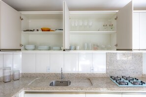 A kitchen with white cabinets, a granite countertop, a stainless steel sink, and a gas stove. - Apto com Churrasqueira a 400m da Praia Gravat (Navegantes)