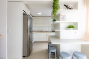Une cuisine moderne avec des meubles blancs, un réfrigérateur en acier inoxydable et un coin bar équipé de tabourets.