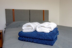Un lit avec une tête de lit grise, deux oreillers et une pile de serviettes pliées.