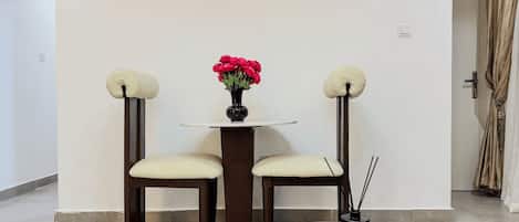 A minimalist room with a round table, two chairs, a vase with flowers, a book, and a decorative object on the floor.