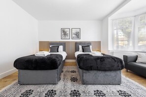 A hotel room with two beds, a grey sofa, a patterned rug, and a window with a view. - Spacious Home, Sleeps 12, Great Transport Links (Southall)