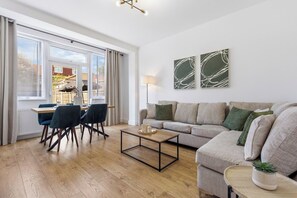 A modern living room with a sofa, a coffee table, and a dining area with chairs. - Spacious Home, Sleeps 12, Great Transport Links (Southall)