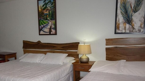 A hotel room with two beds, a nightstand with a lamp, and two paintings on the walls. - HOTEL LEON INN (León)