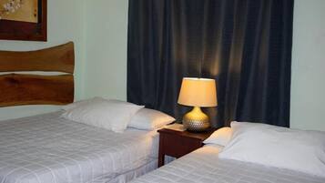 A hotel room with two beds, a wooden headboard, a dark curtain, and a table lamp.